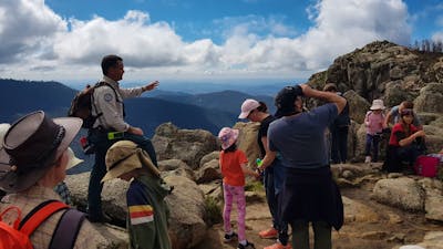 Ranger and children seated on rocks with mountain range in the background.