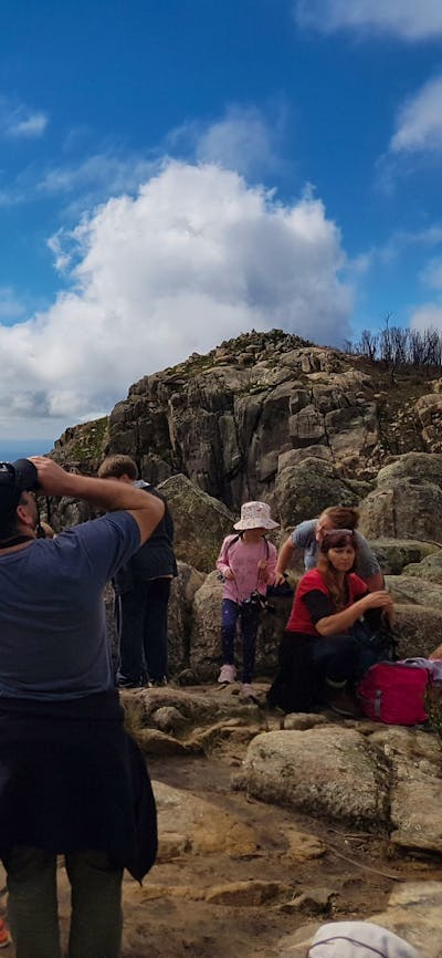 Ranger and children seated on rocks with mountain range in the background.