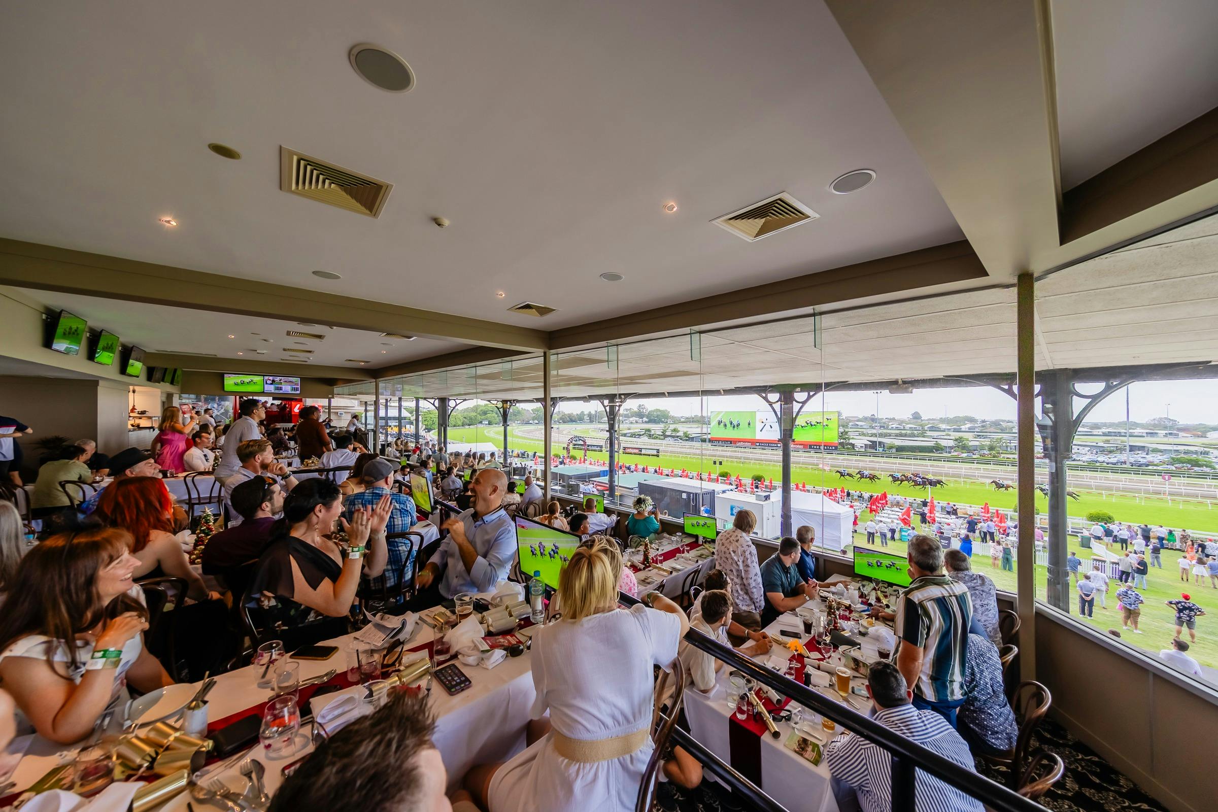 People at dining tables watching horse races through glass wall