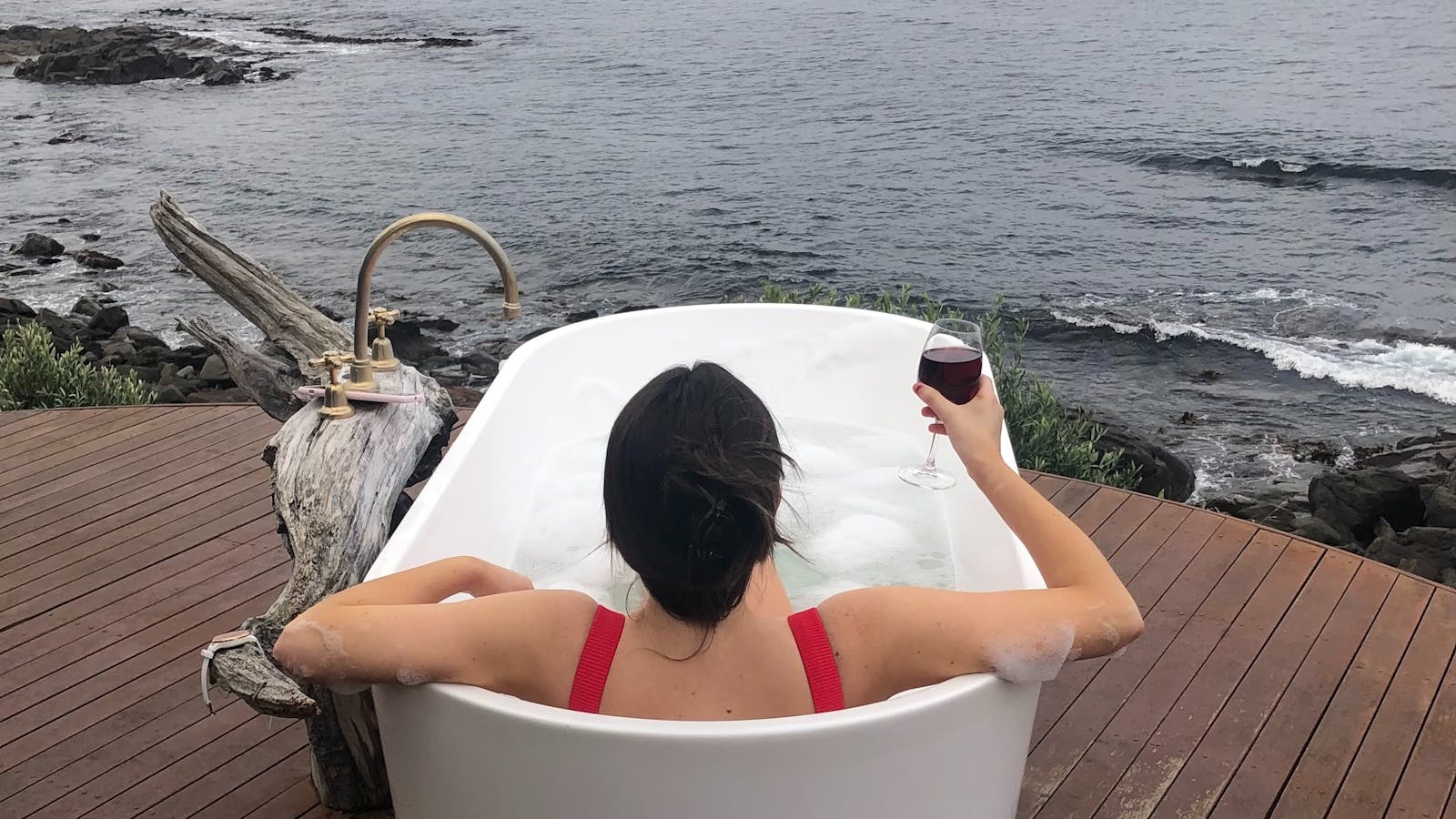 in a bathtub on a cliff, gazing at the ocean under a glowing sunset — peaceful and surreal.