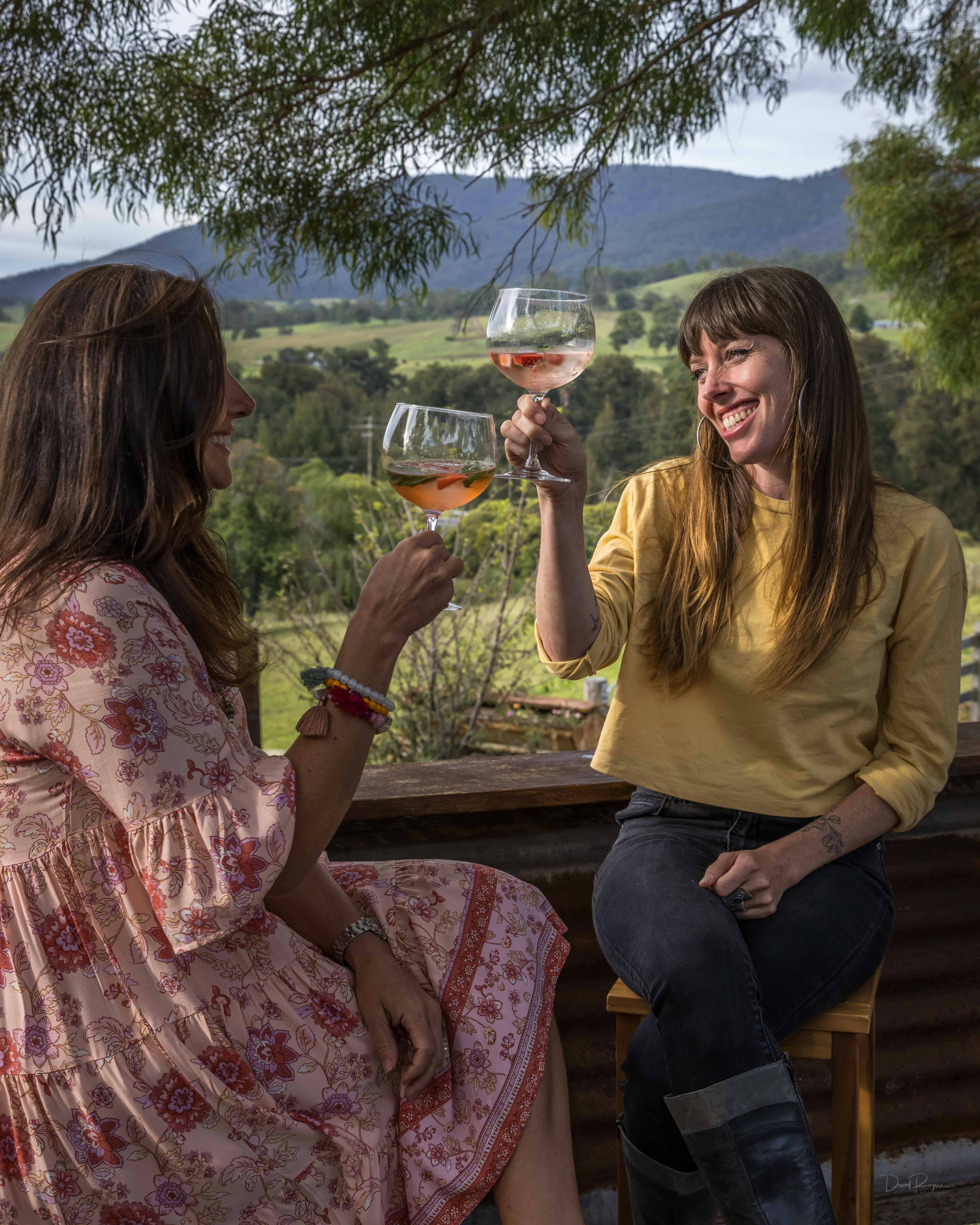 Two women toasting each other against a country backdrop
