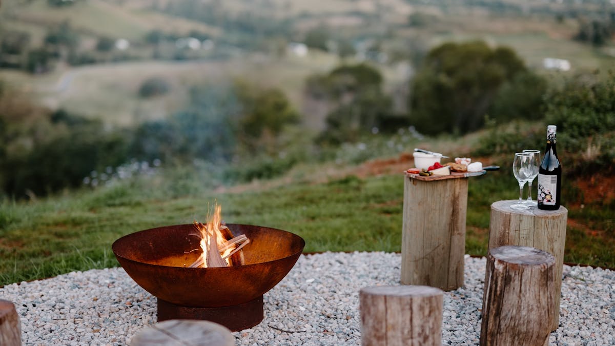 Photo of a firepit with blazing fire, wine & cheese platter with views of rolling hills & Brisbane
