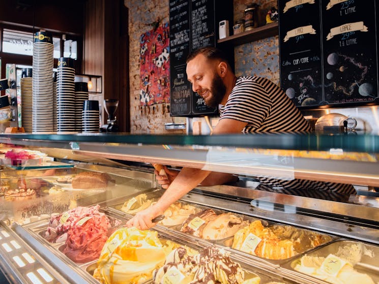 Man scooping gelato for a customer at Cow and The Moon artisan gelato store on Enmore Road, Enmore