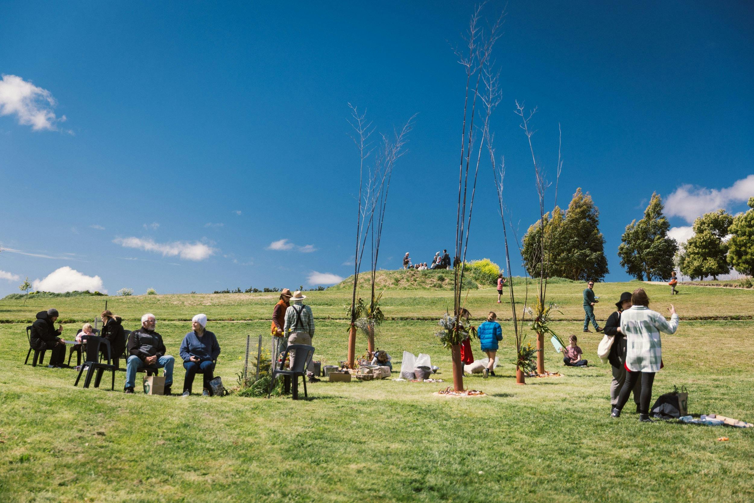 People are sitting or standing chatting in a green grassy area with a stunning blue sky.