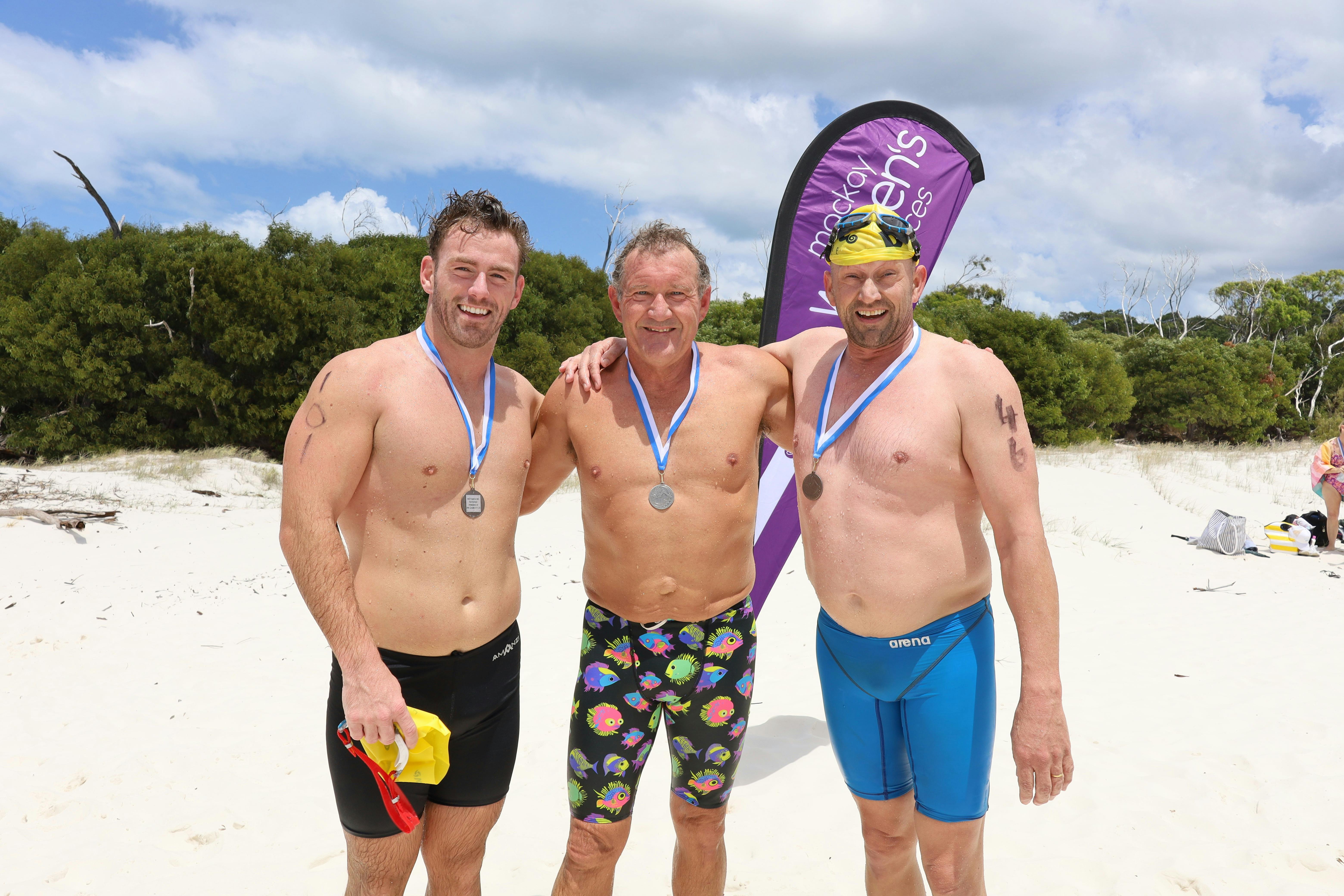 three men with medals around neck smiling for camera after swimming 2km
