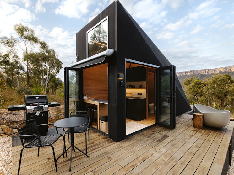 Architectural design, this tiny house opens up onto a surrounding deck with BBQ, table and chairs.