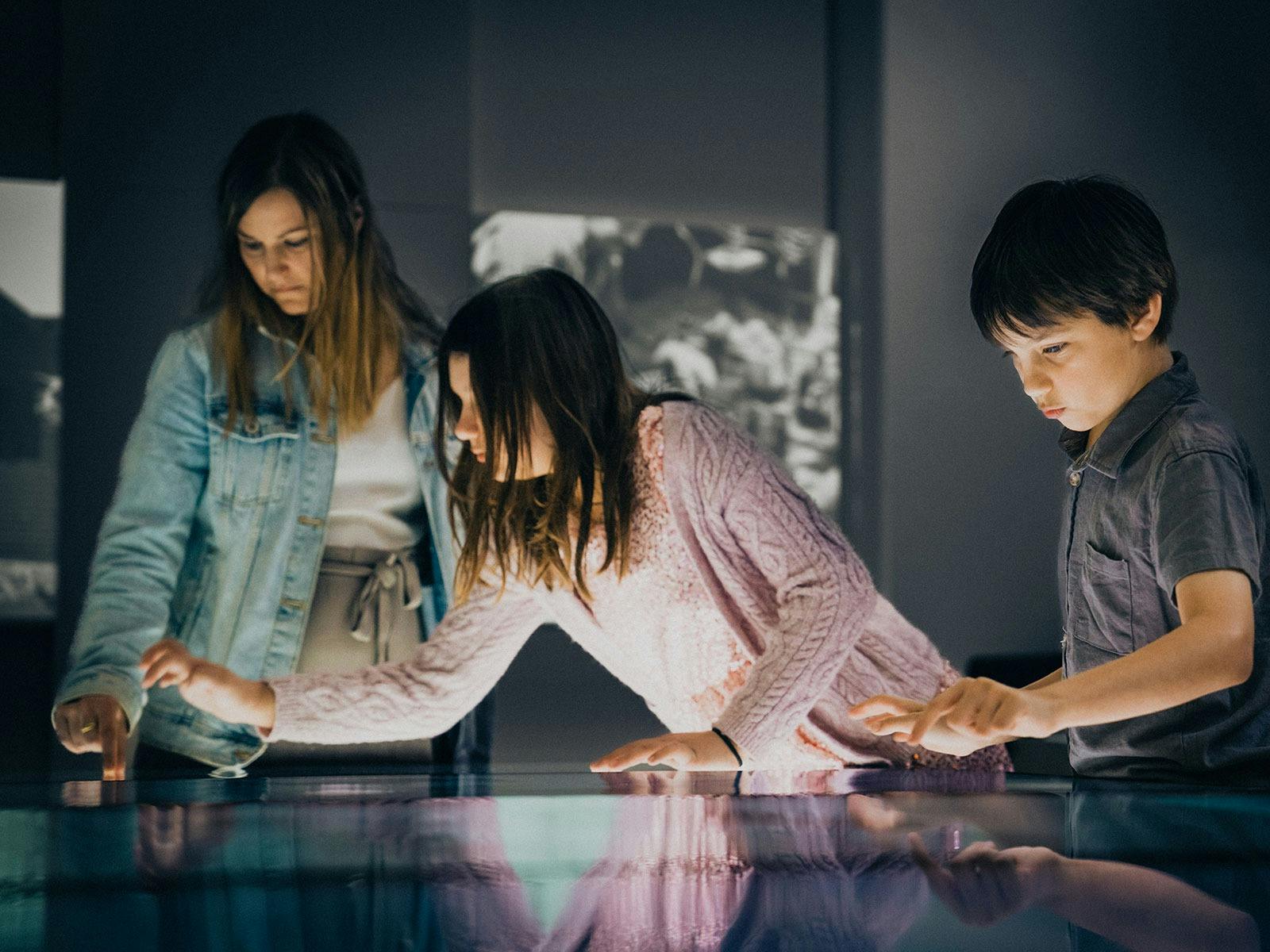Young family using the interactive screens inside the World War II Gallery at Anzac Square