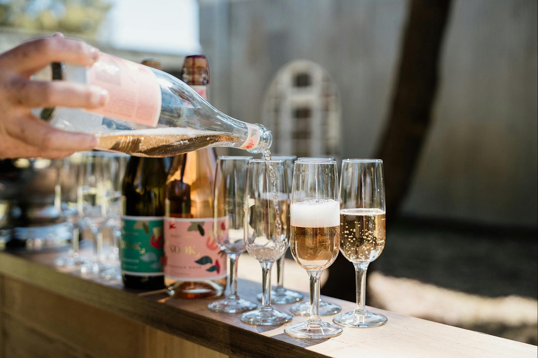 Pouring a glass of Rosé Prosecco, with other glasses of Prosecco already poured, placed on a timber