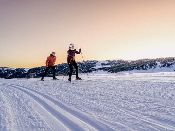 Two people cross country skiing in the sunset