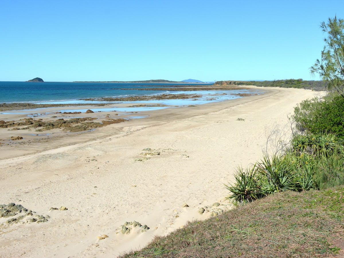 Sandy beach looking over rock intertidal zone with ocean and islands in the background.
