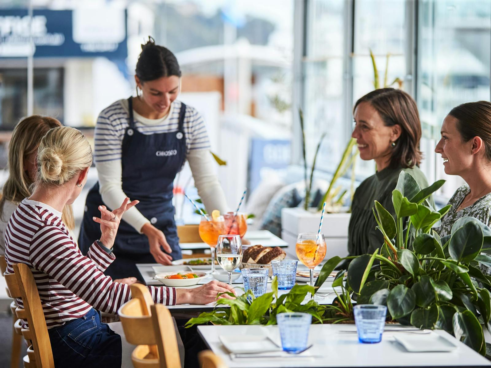 A group of 4 guests dining at Chiosco with Aperol Spritz and an attentive waiter serving them