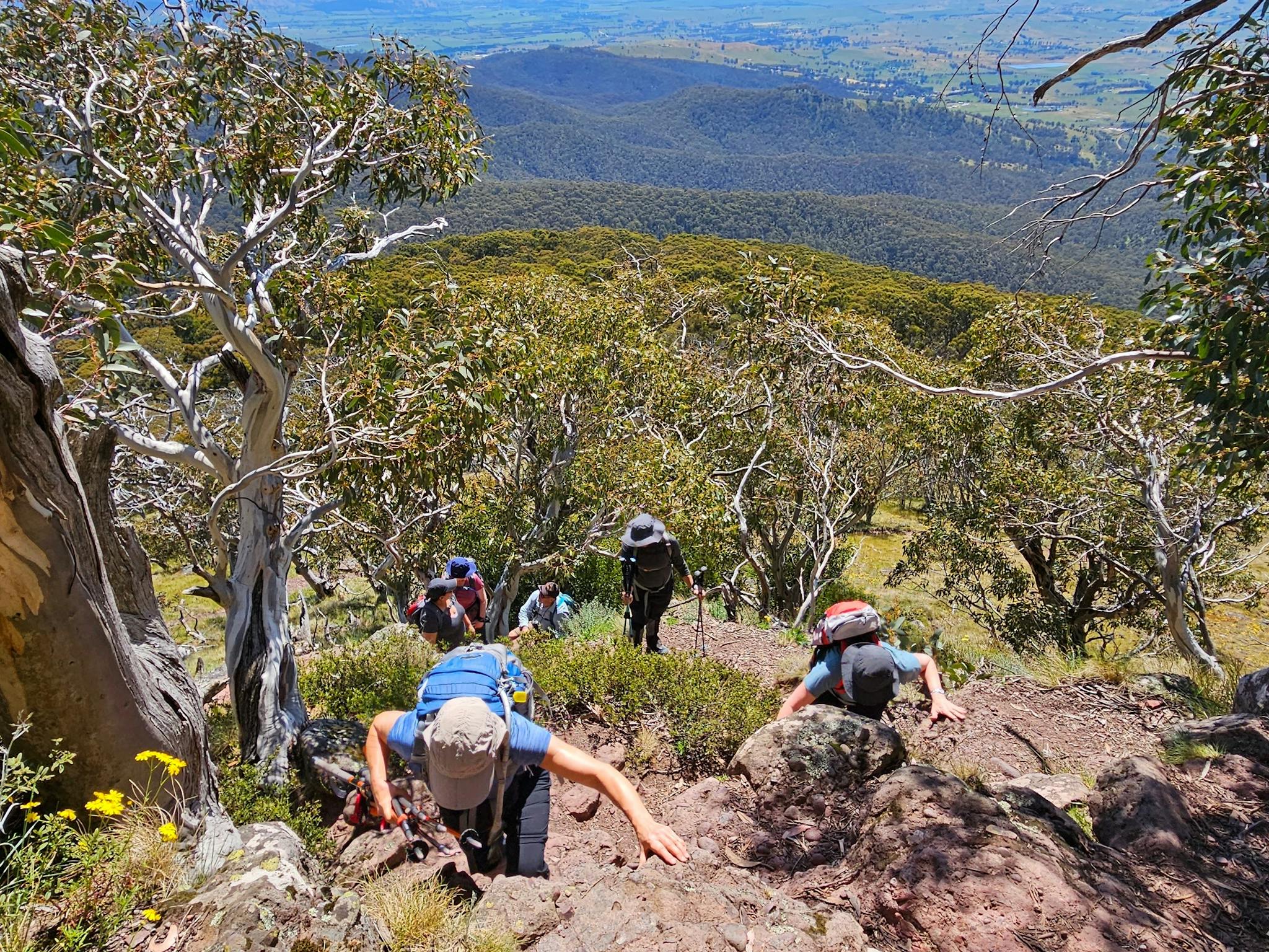 Hikers are scrambling up a rocky outcrop.