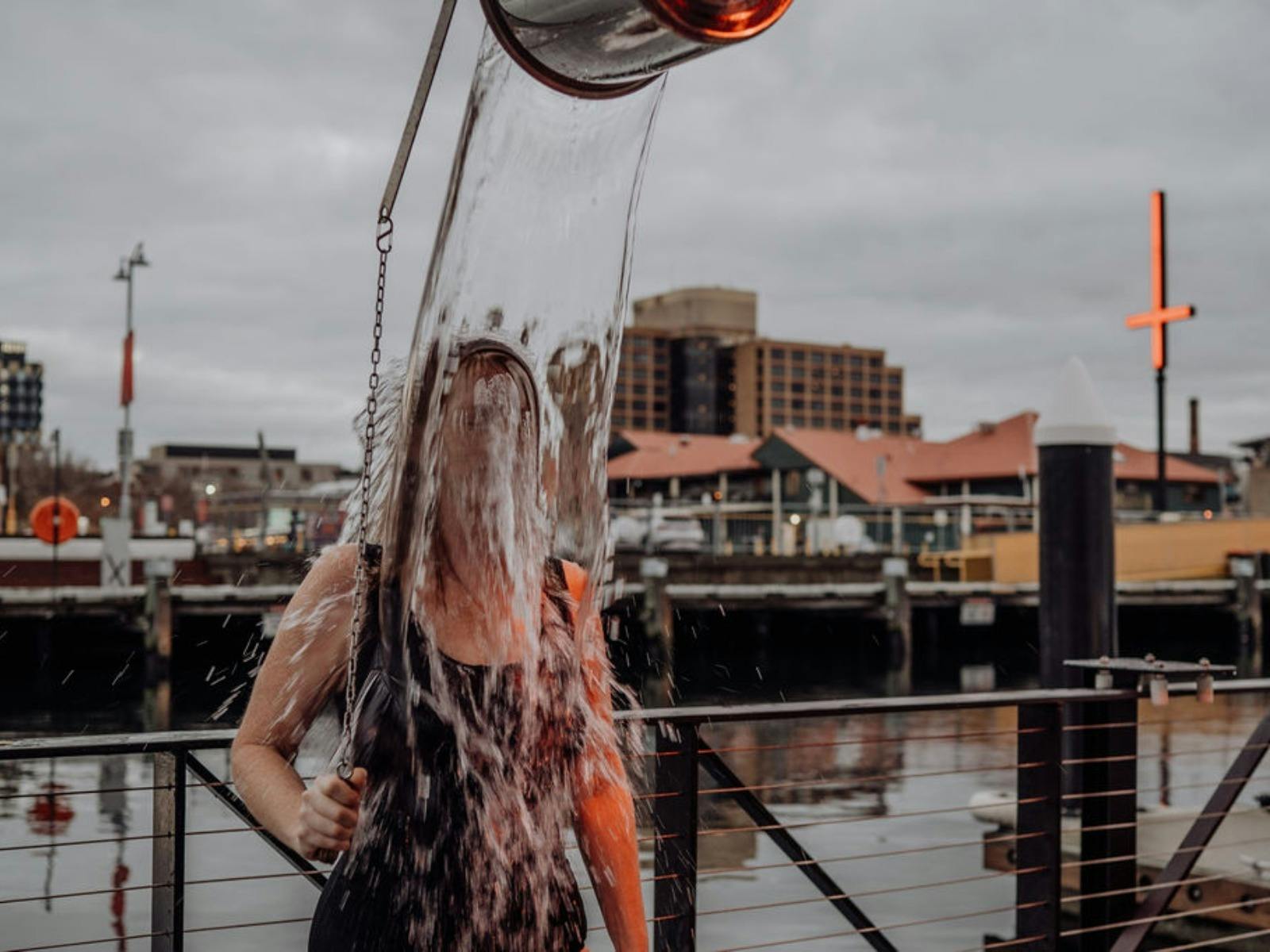A person on a harbor pier stands under a pouring bucket shower.