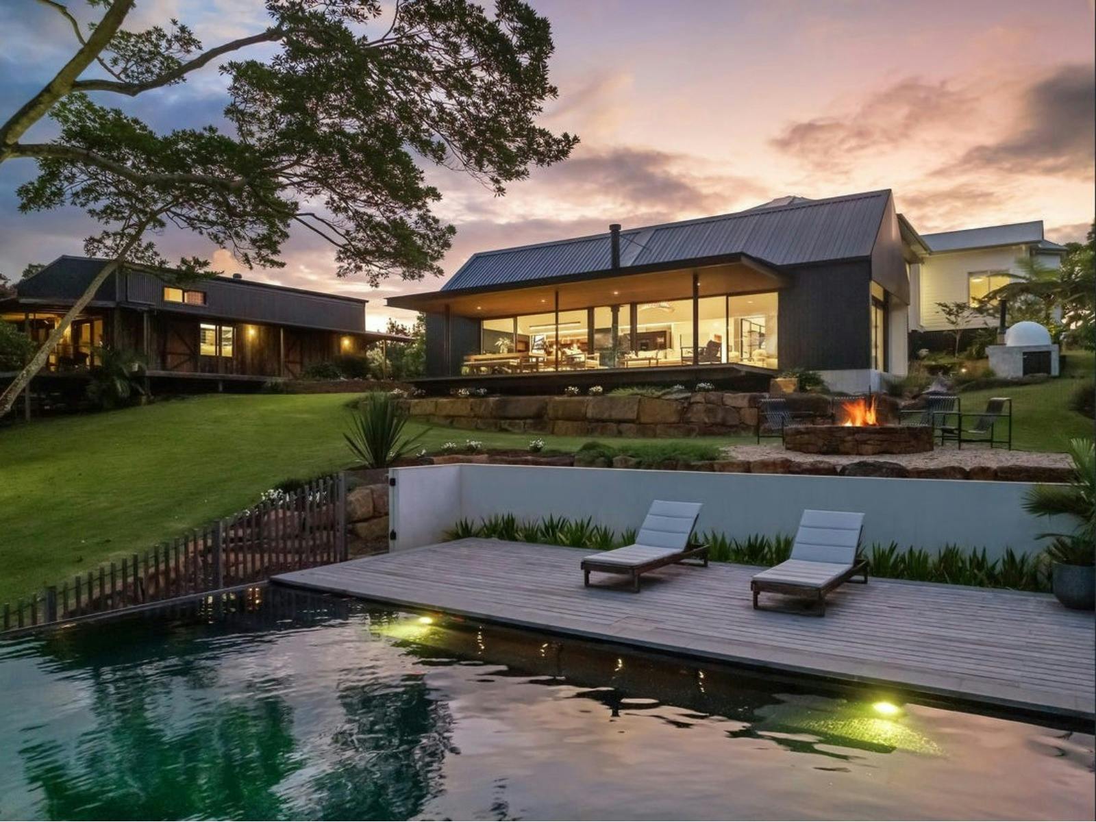 Infinity pool overlooking Charlotte Estate with fire pit and illuminated pavilion at sunset.