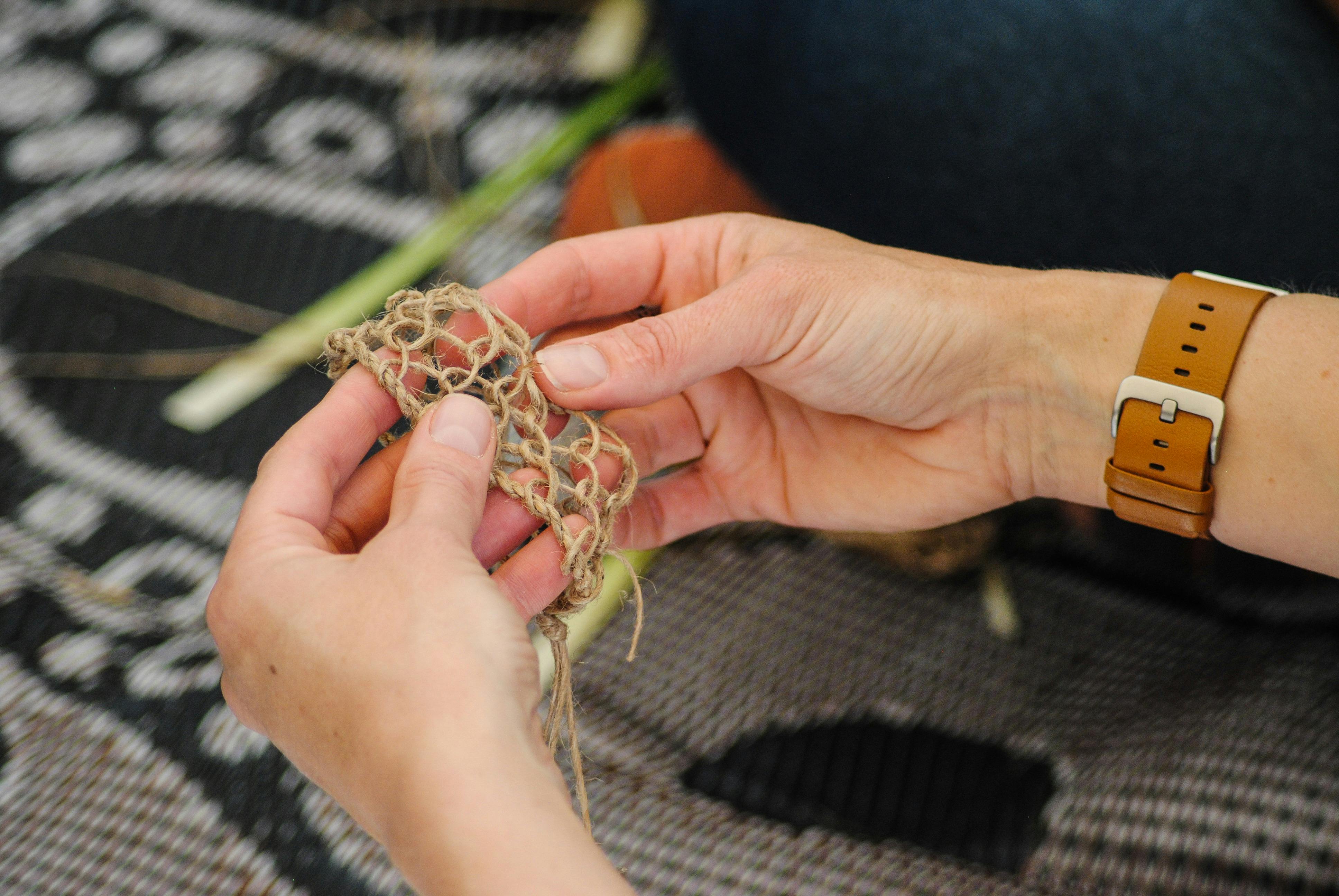 Hände halten ein gewebtes Armband aus Naturmaterialien.