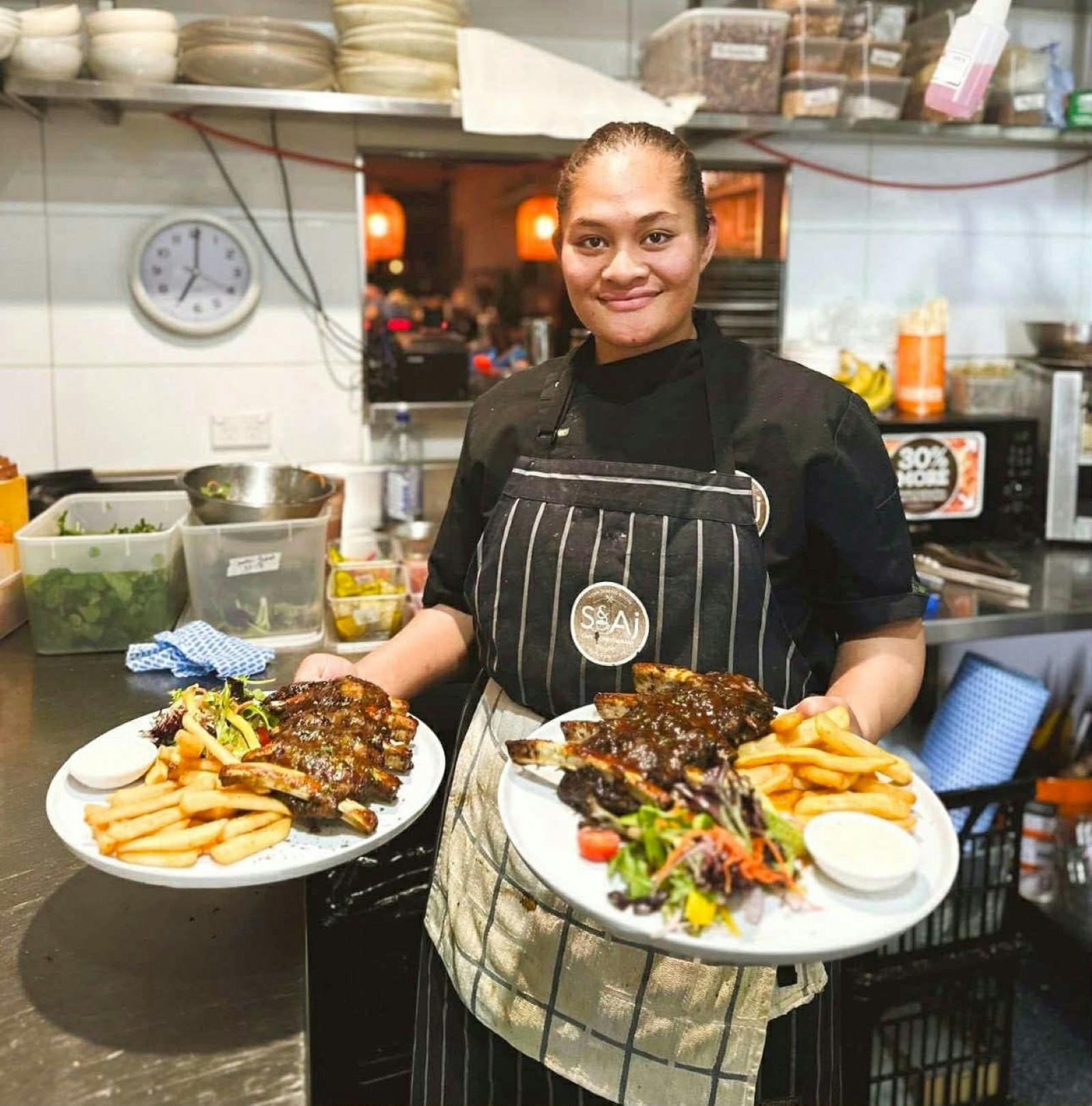 One of the chefs holding two full plates of ribs, chips and salad.