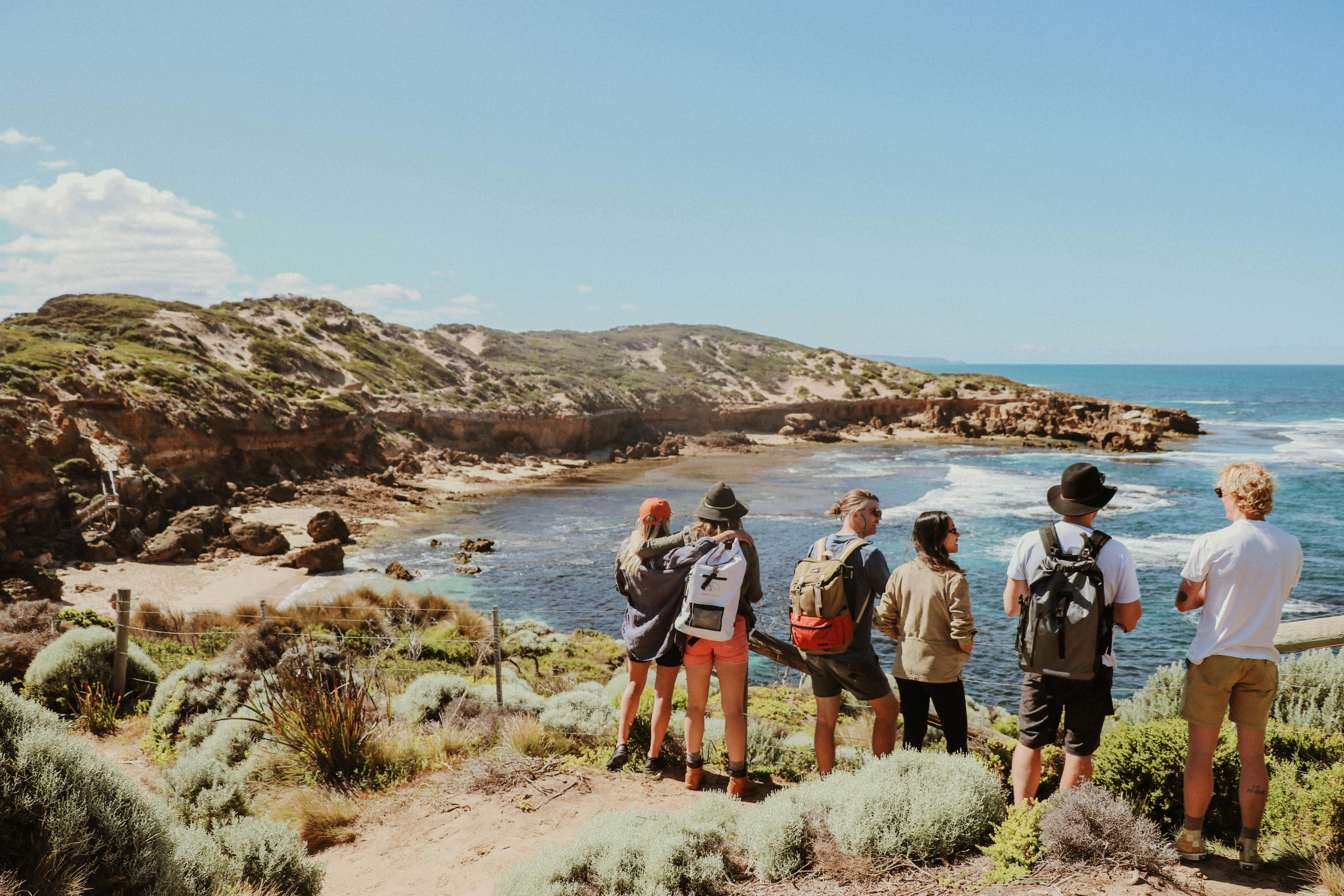 Group with backpacks standing at ocean viewpoint with backs to camera