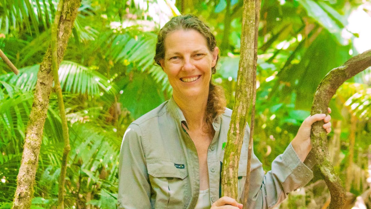 Forest Therapy Guide smiling and standing in the rainforest holding a vine