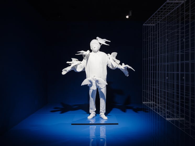 A white statue made of resin of a Chinese migrant worker with birds rested on him, in a blue room