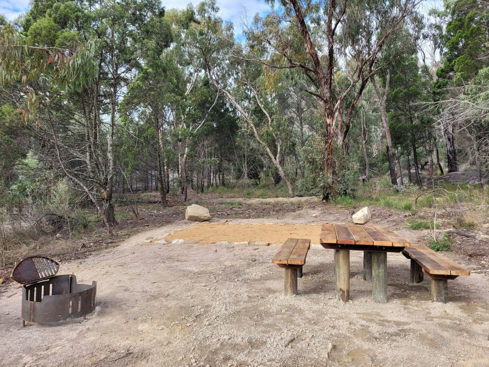 A flat, dirt camp site, featuring a fire pit and picnic table. A flat, dirt camp site, featuring a fire pit and picnic table.