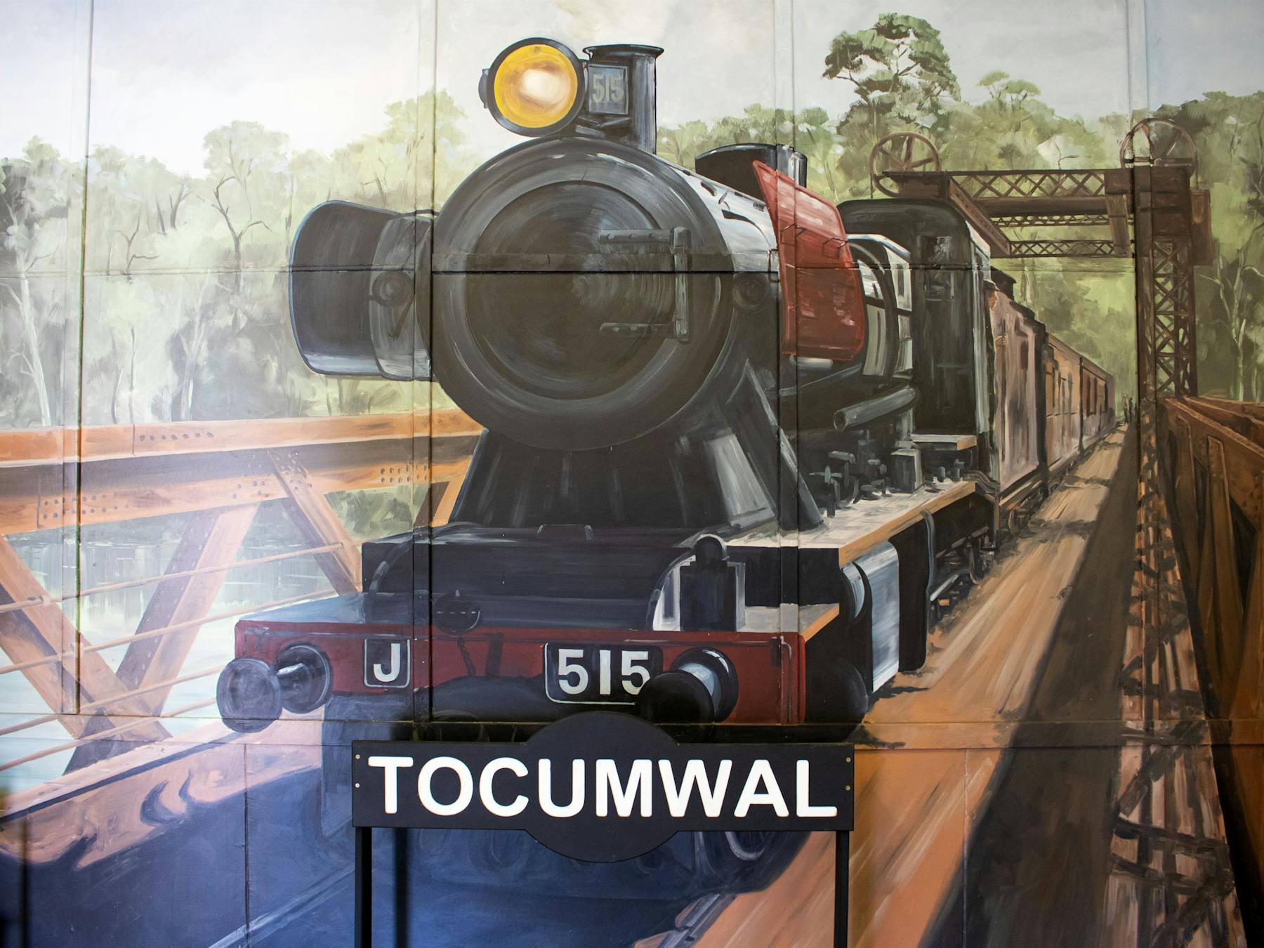 Mural of steam engine crossing bridge, with a railway station sign saying 'Tocumwal' in front.