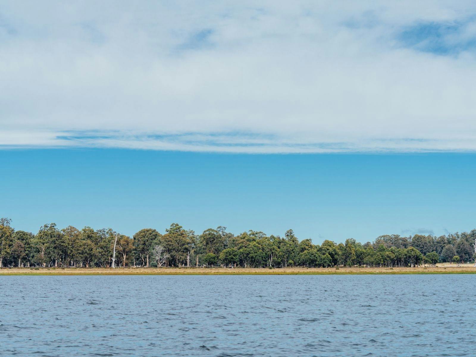 A still lake with a shoreline and trees in the background