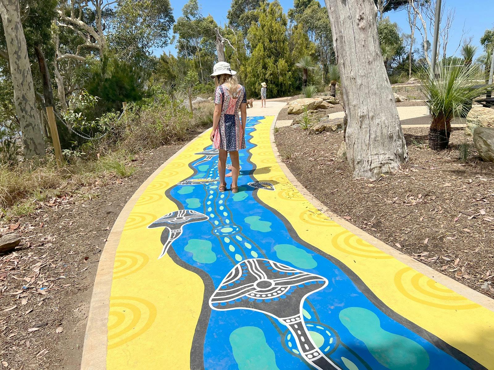Child on a pathway painted with a colourful mural with aboriginal designs