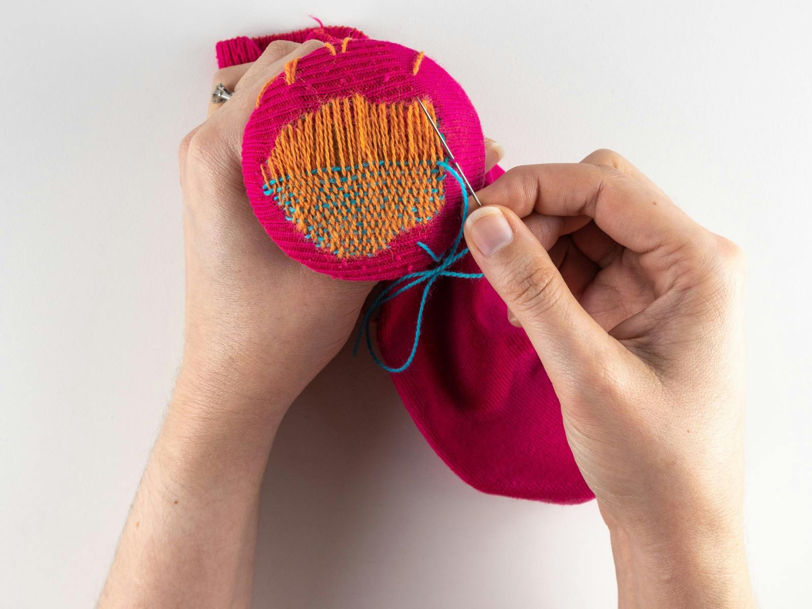 Two hands sewing heel of an orange and pink sock
