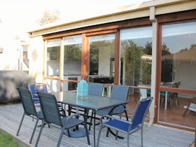 Image of outdoor entertaining area with table for 6 and bbq, looking into kitchen through full glass