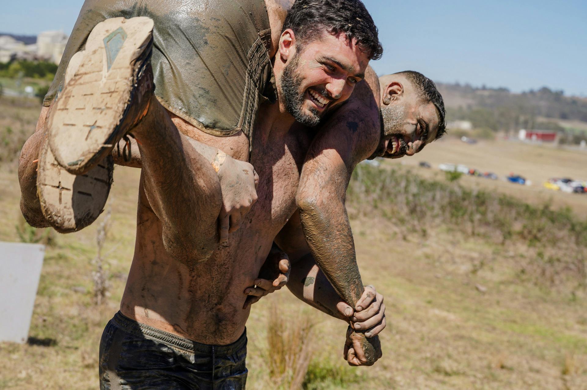One Mudder carrying another Mudder over his shoulders