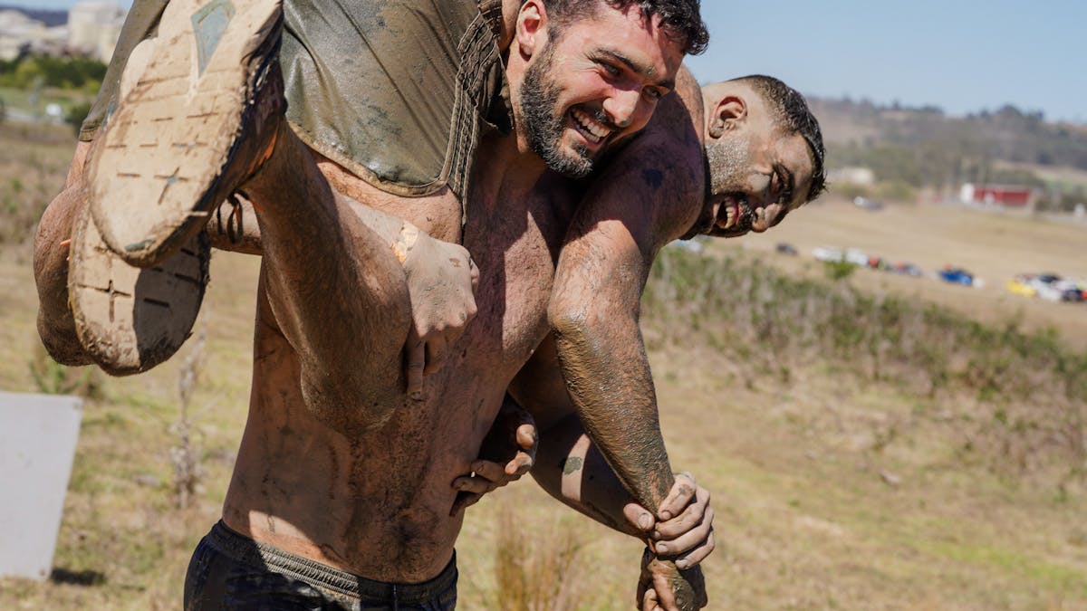 One Mudder carrying another Mudder over his shoulders