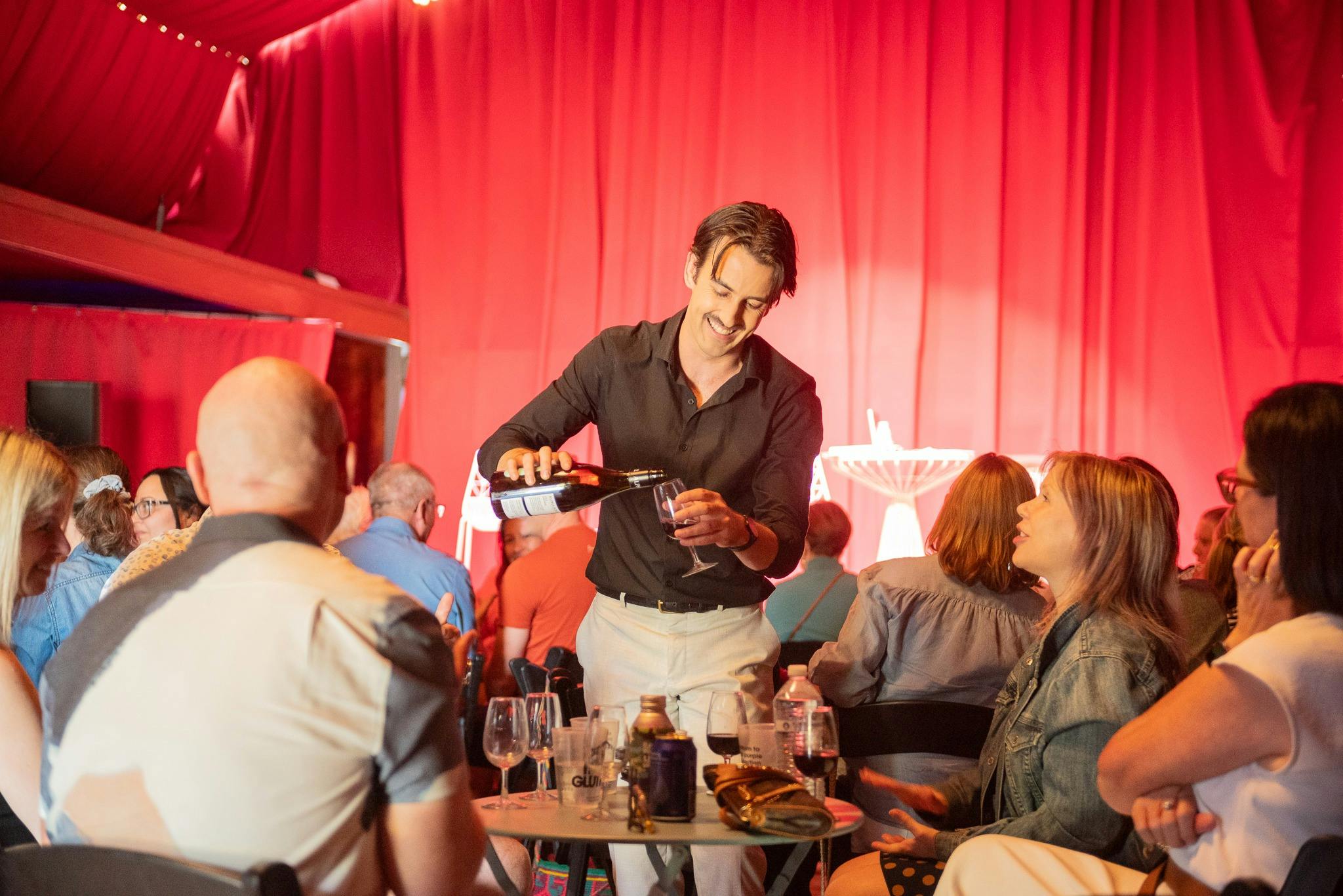 Man standing pouring wine while laughing with people seated at table