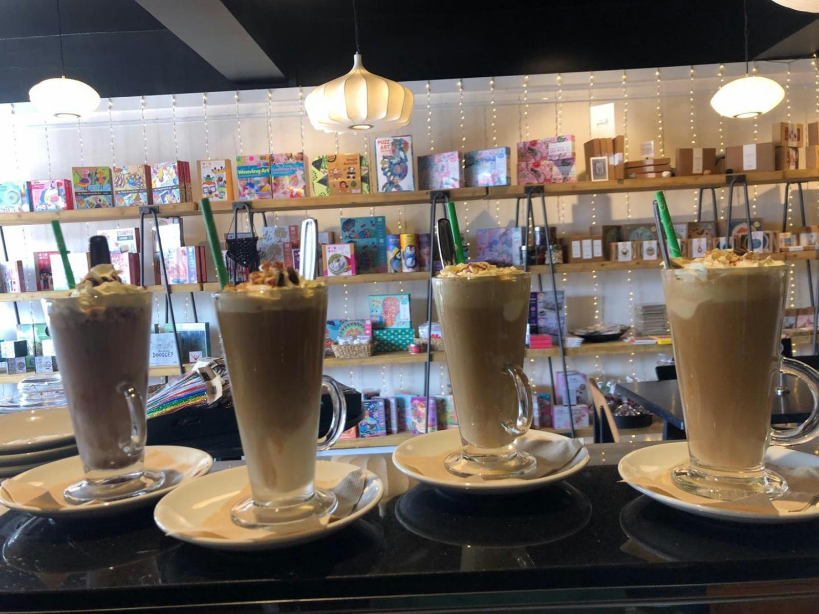 Four iced coffee drinks in tall glasses topped with cream sitting on the counter ready for customer