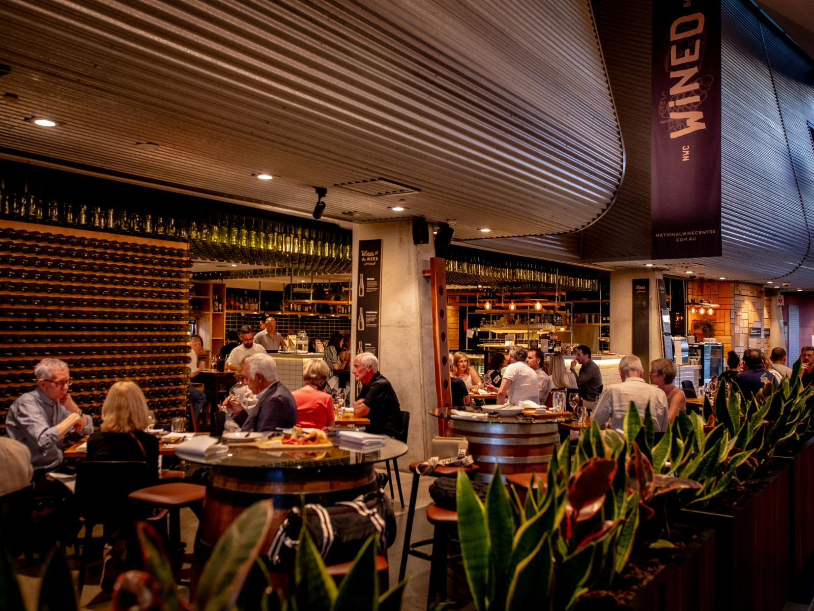 Busy wine bar and dining room with seated guests and wine displays.
