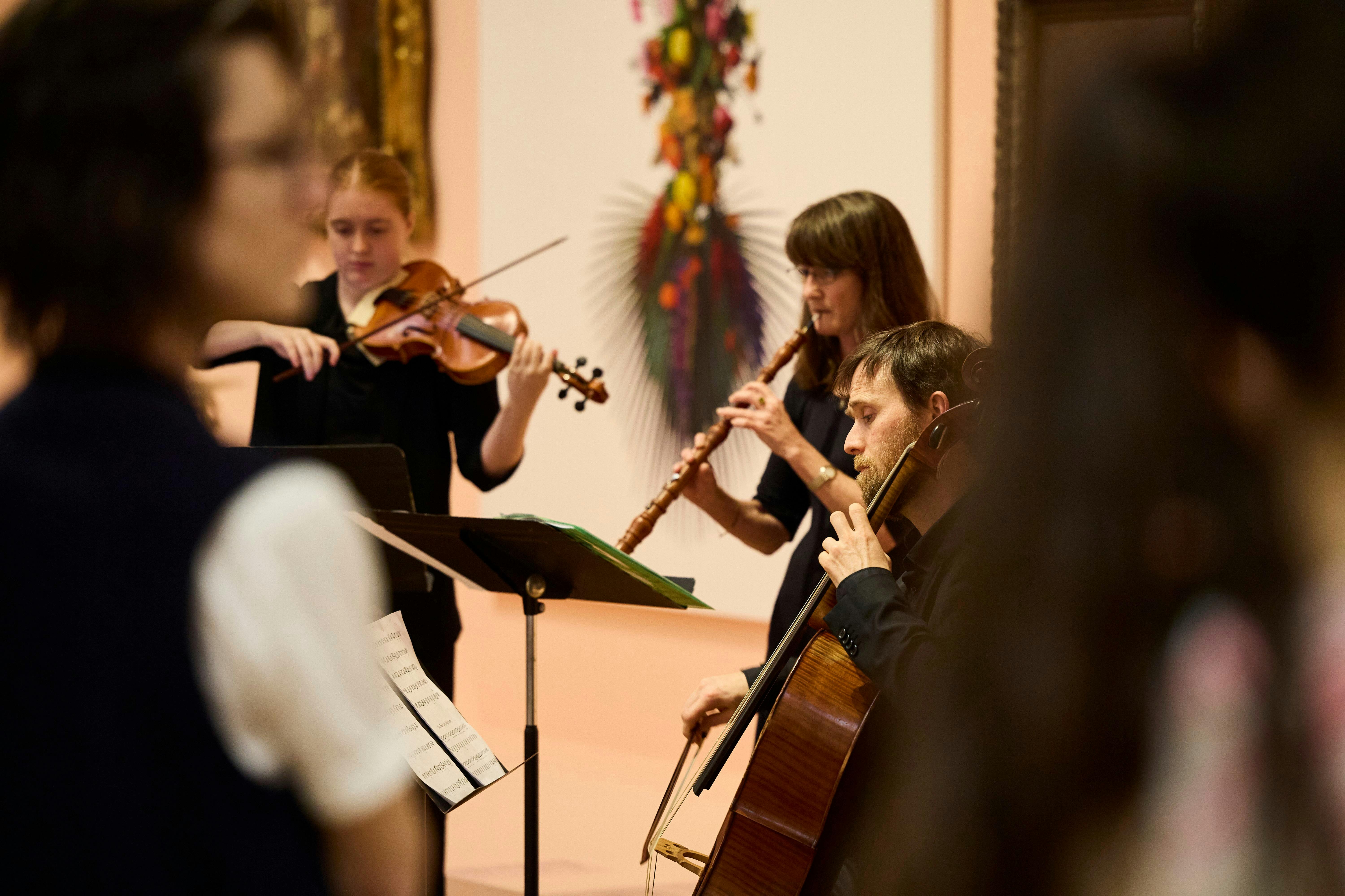 A small ensemble of musicians perform in an art gallery for an audience of standing onlookers.
