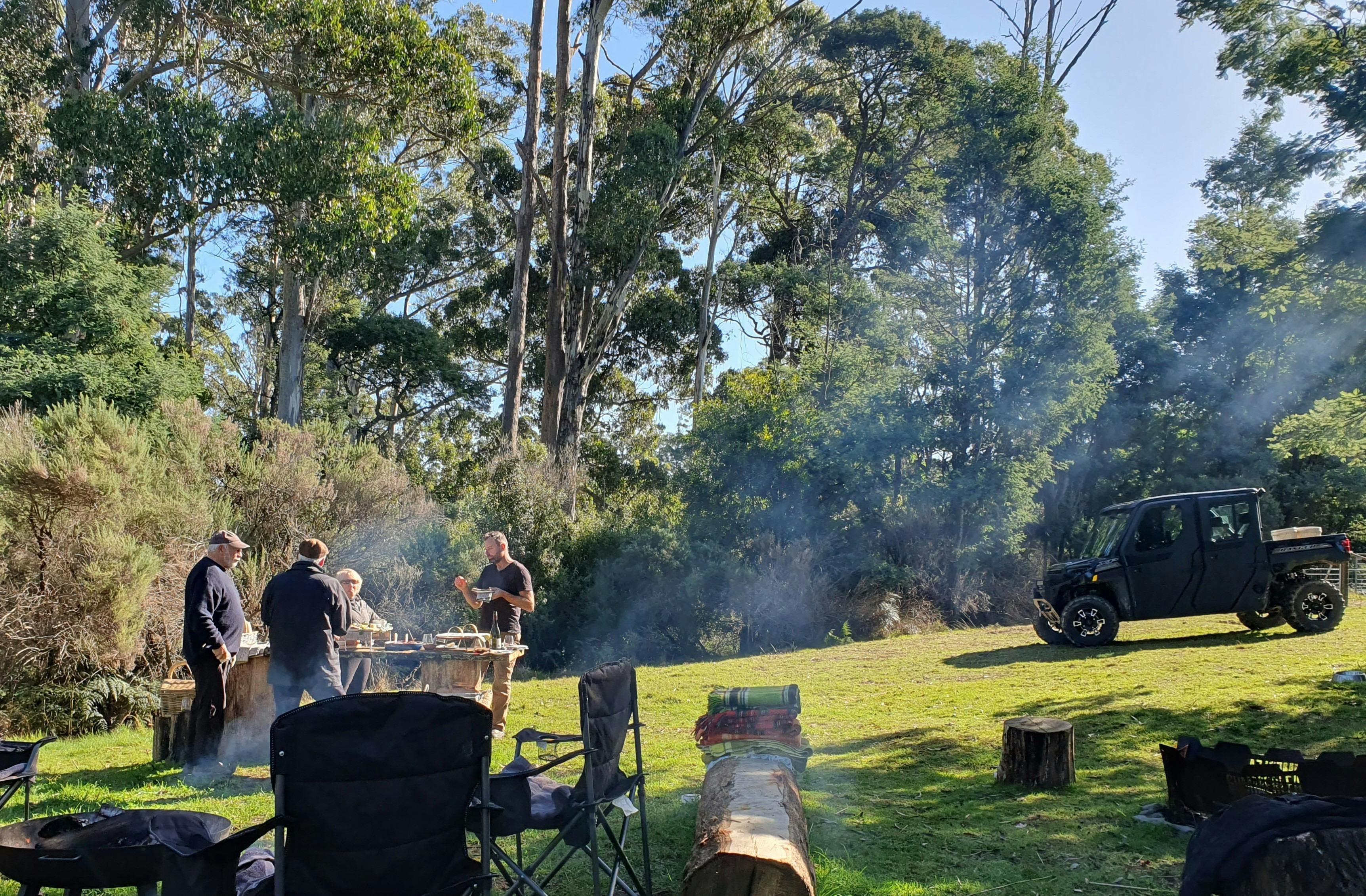 four people standing together enjoying a picnic platter with bushland and Polaris allterrain vehicle