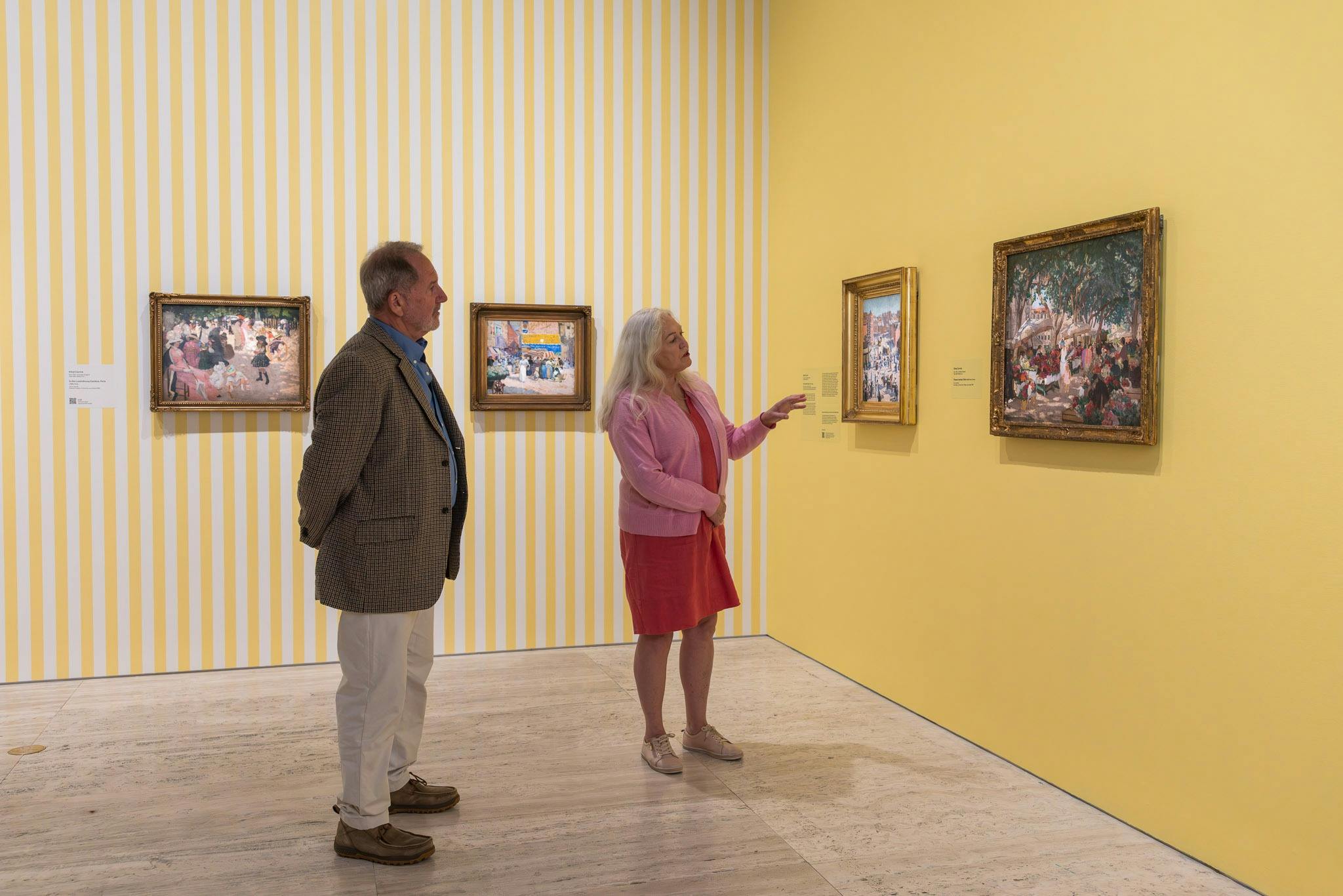 An older man and woman looking at two paintings in an art gallery
