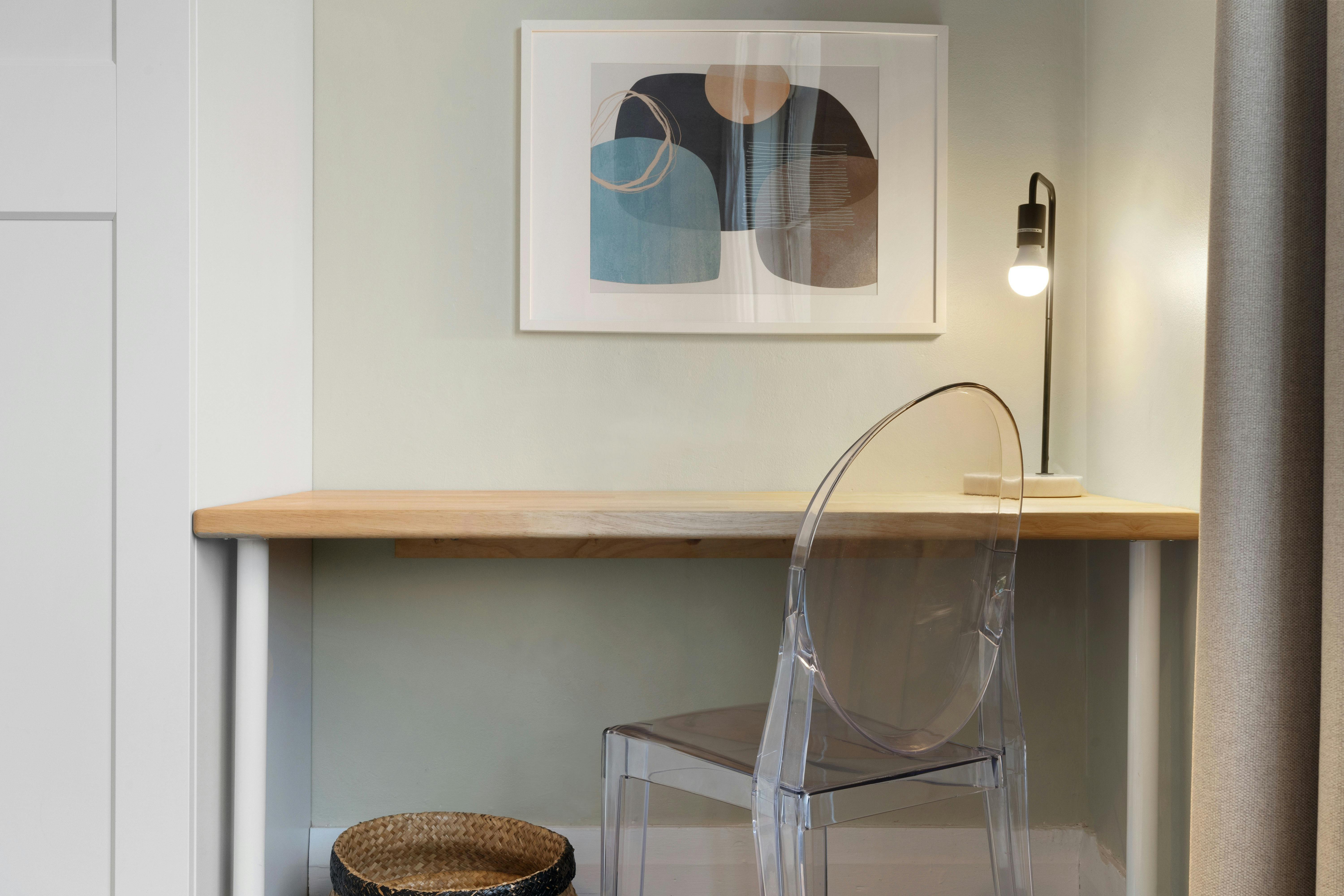 Minimalist study nook with a transparent chair and wall art.
