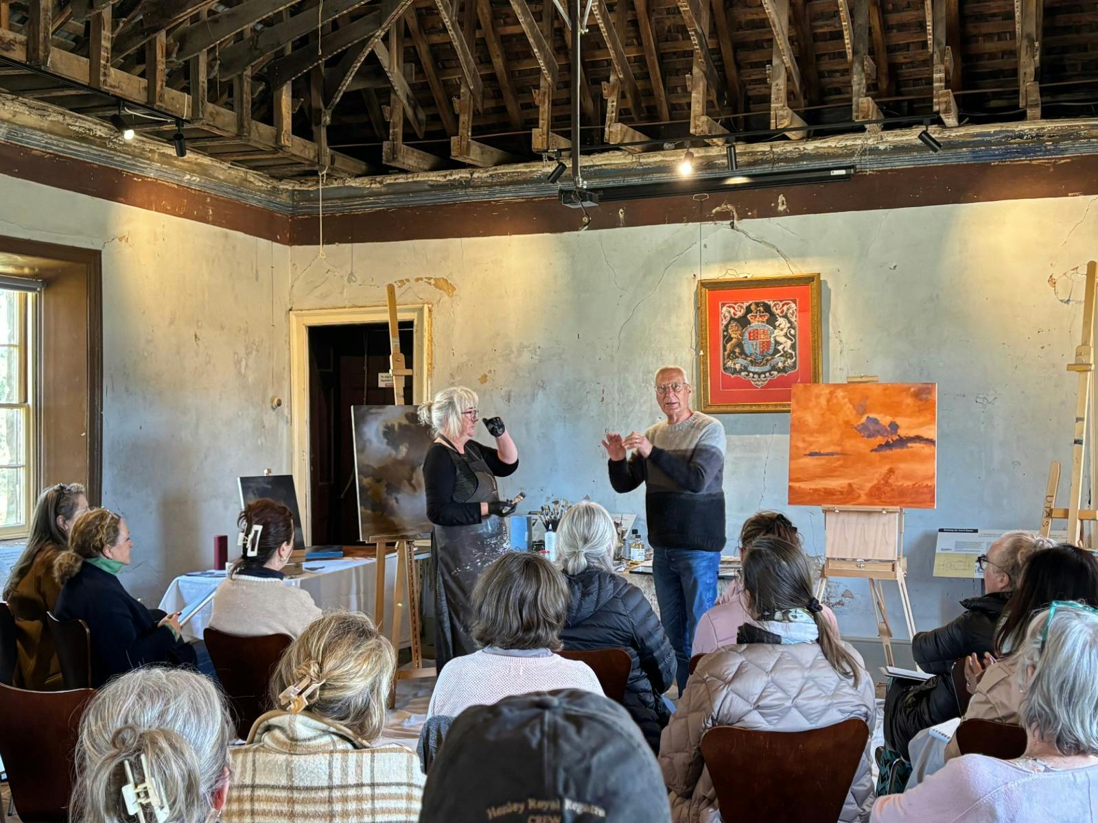 A group of people sit in a historic old building, listening to two people talk