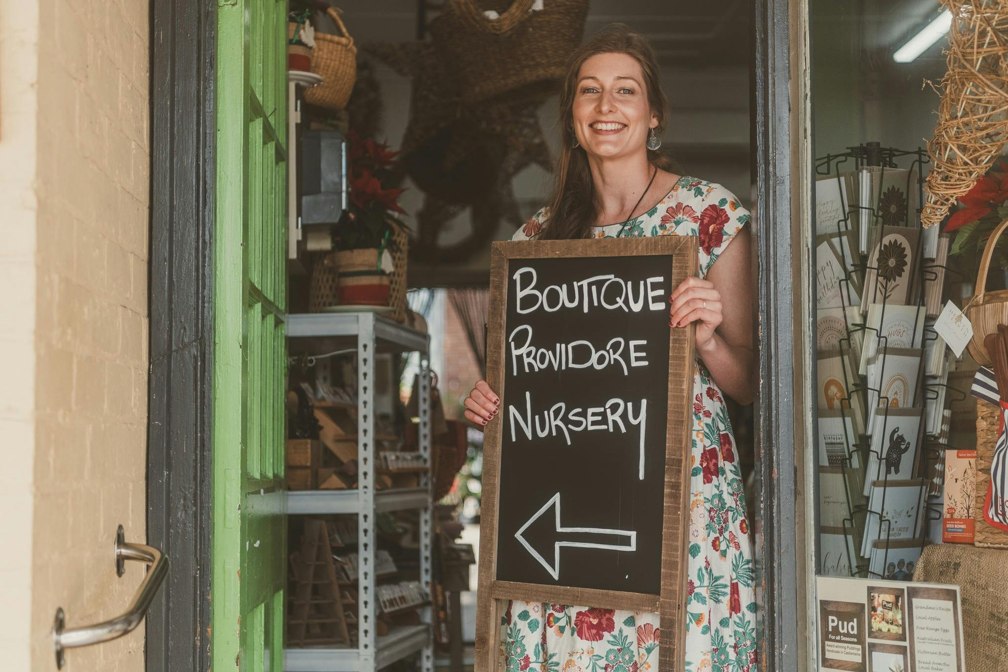 woman holding sign that says, boutique, providore, nursery