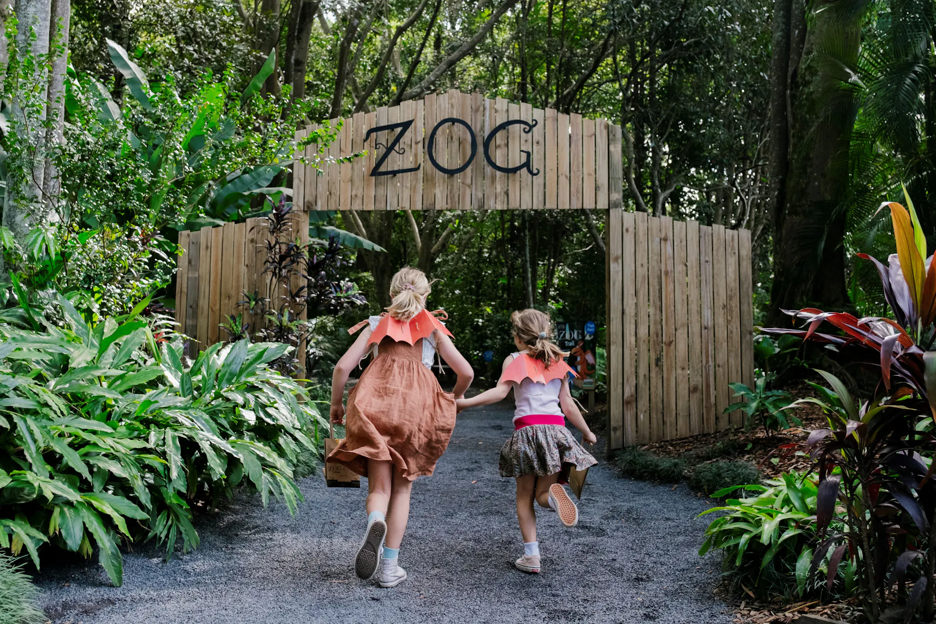 Two girls running through the entrance of the Zog: A Forest Adventure Trail wearing dragon wings