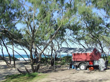 A red camper trailer is parked amongst the casuarinas behind the beach, A red camper trailer is parked amongst the casuarinas behind the beach,