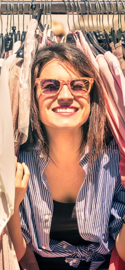 two women smiling peeking through a rack of clothes at an outdoor market