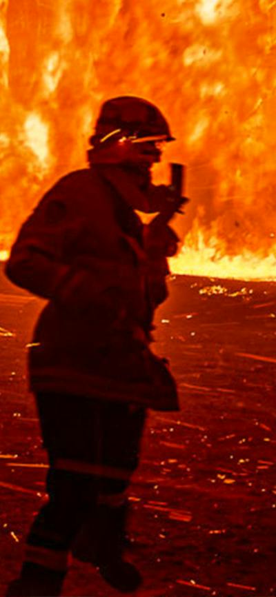 Firefighters in the midst of burning bush with fire truck in the background