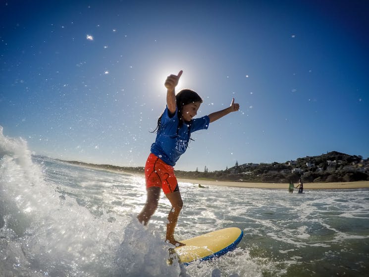 This young girls has her thumbs up to her surf lesson