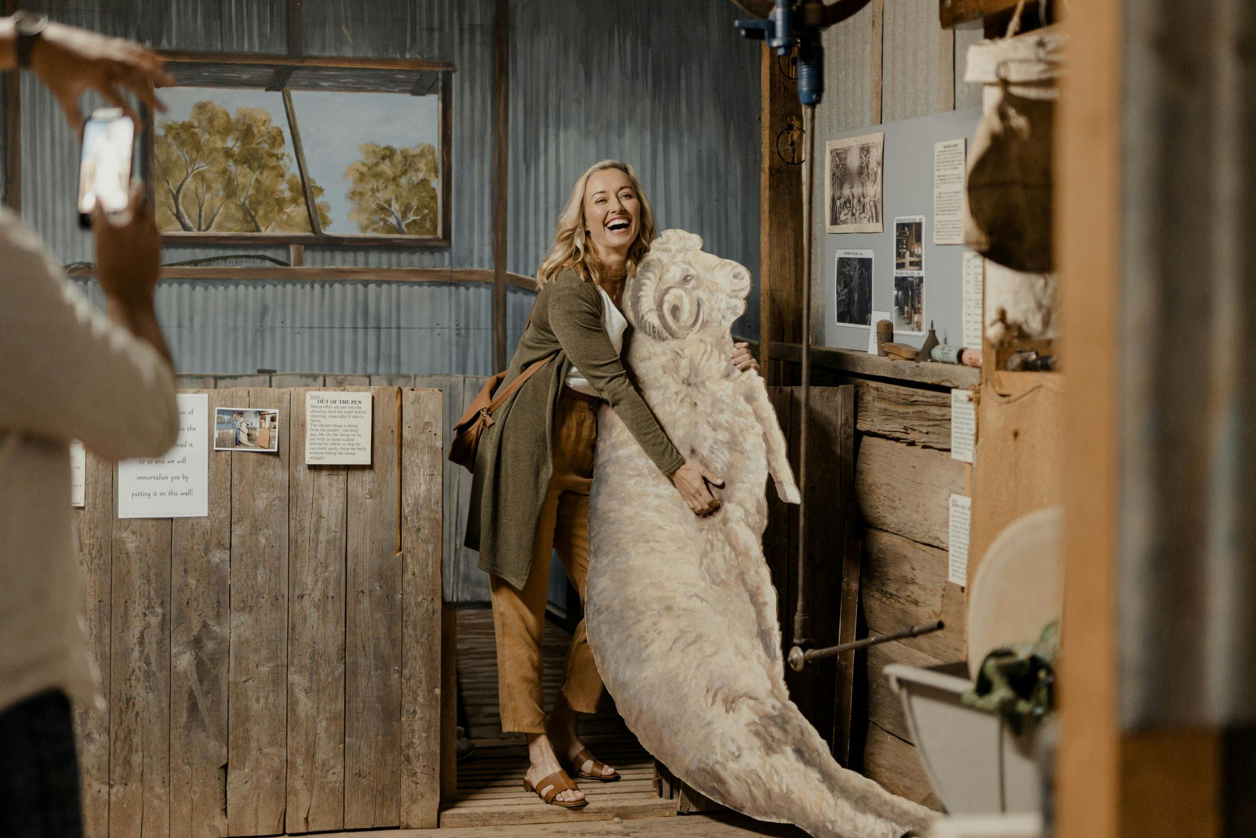 A blonde woman hugs a lifesize cutout of a sheep in a museum.