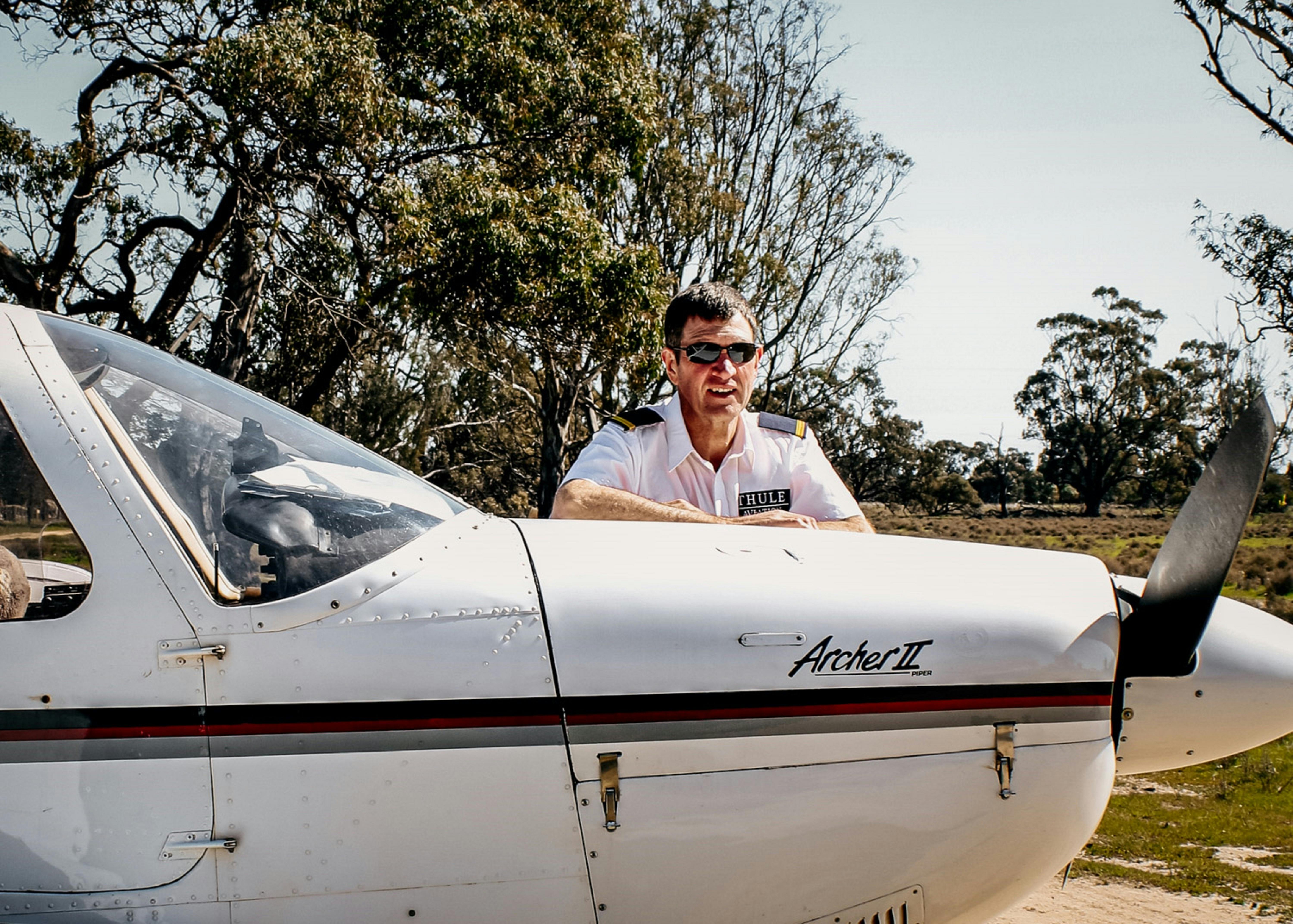 Pilot Peter McDonald standing next to aeroplane with gumtrees in background.