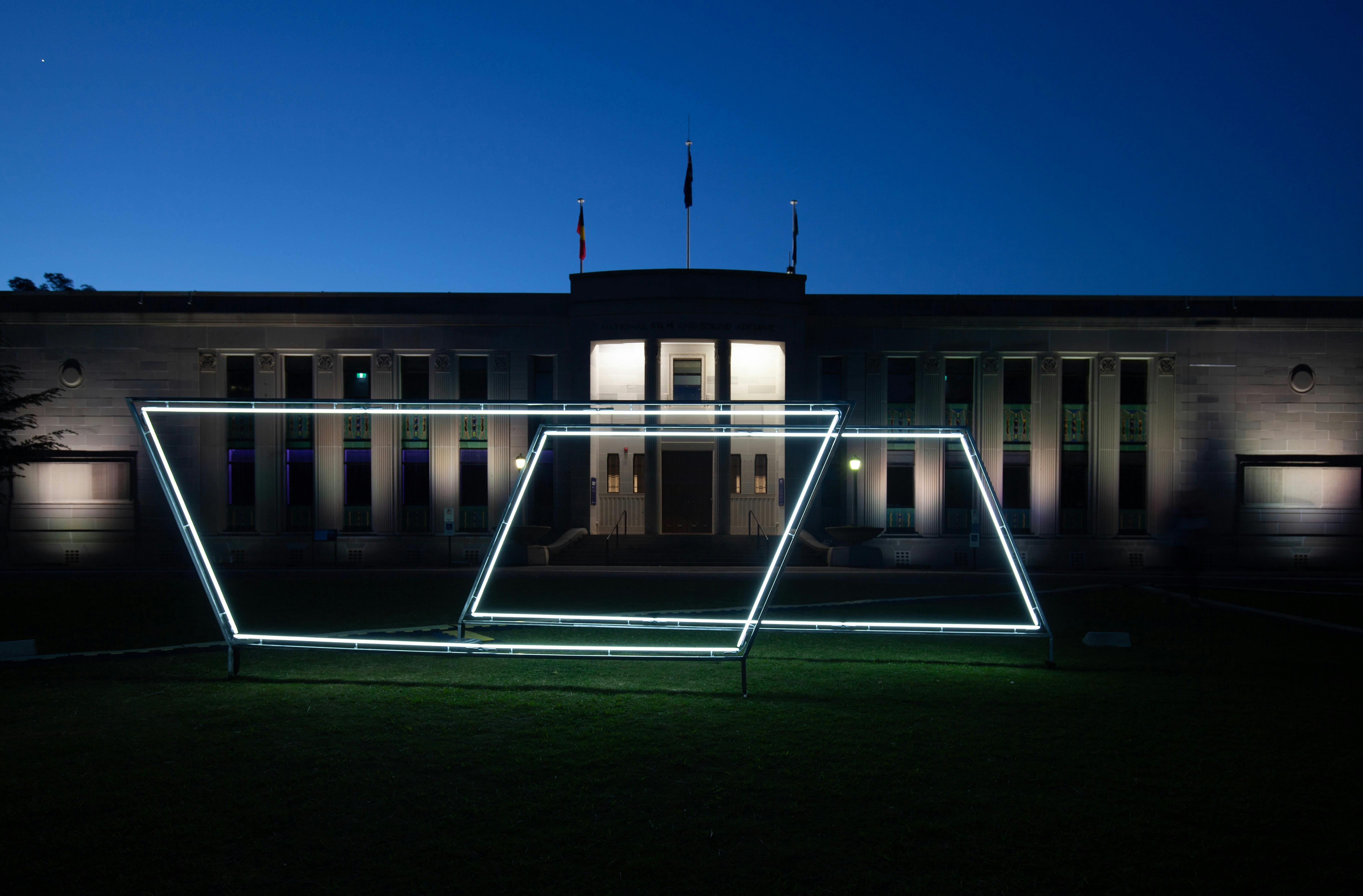 Neon light sculpture on the grass of the National Film and Sound Archive. Photo taken at night.