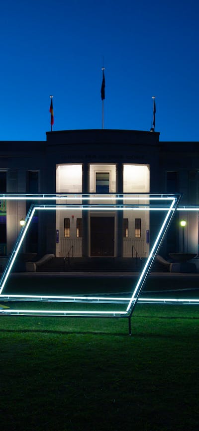 Neon light sculpture on the grass of the National Film and Sound Archive. Photo taken at night.