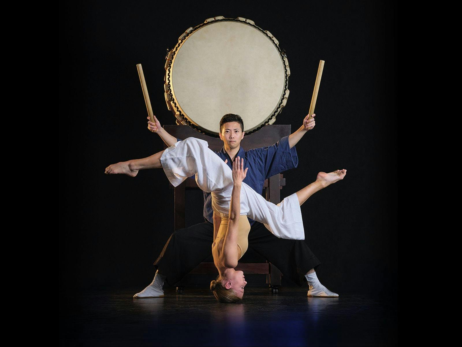 Two performers on stage. One is a dancer and is on their head and the other is a drummer